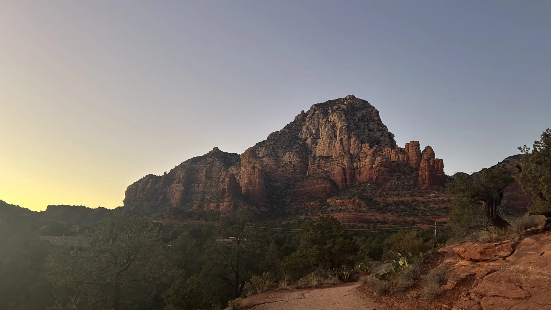 Red rock cliffs above desert shrubs and a rocky trail in warm evening light